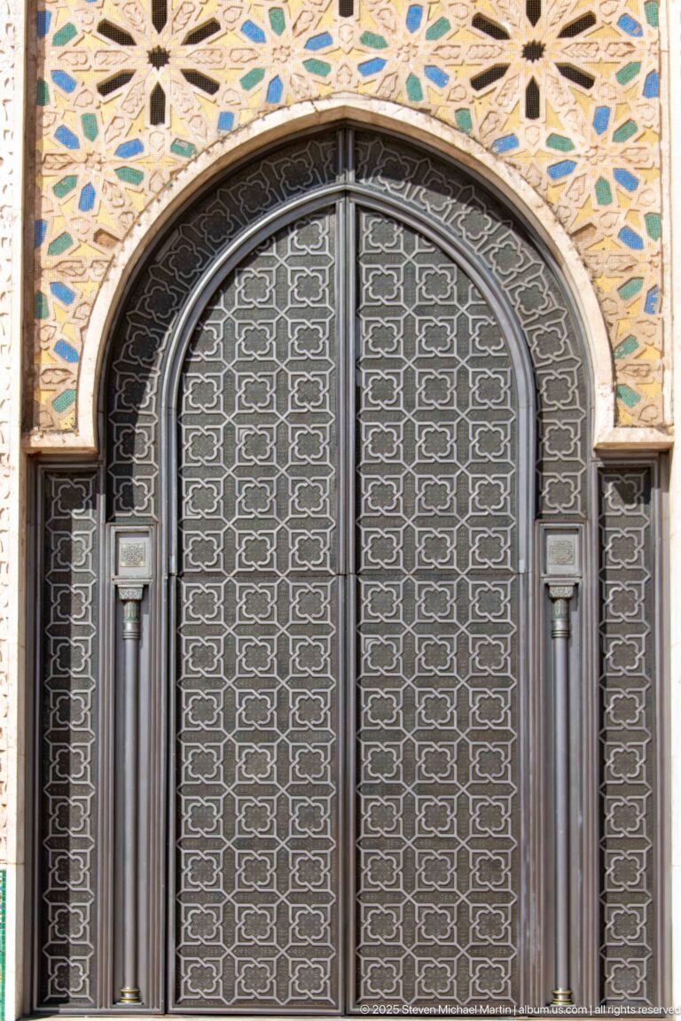 Arched dark metal door with geometric lattice and colorful mosaic ornament above.