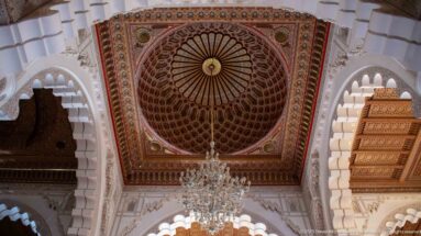 Chandelier below an ornate square ceiling framed by pale horseshoe arches.