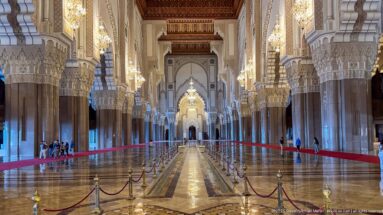 Symmetrical central aisle with stone columns, chandeliers, polished floor, and red barriers.