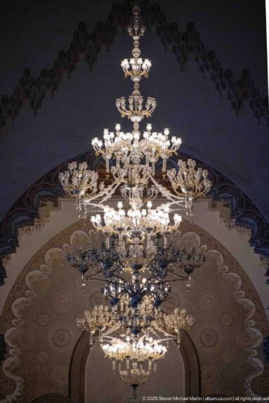 Large tiered chandelier suspended beneath a richly decorated arch inside the Hassan II Mosque.