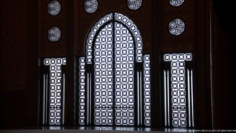 Backlit pointed-arch geometric screen with narrow side panels and circular rosette openings in a dark interior.