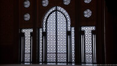 Backlit pointed-arch geometric screen with narrow side panels and circular rosette openings in a dark interior.