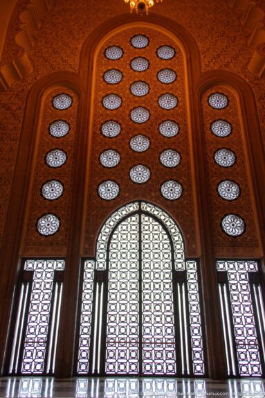 Tall backlit arched screen with circular apertures and narrow flanking screens framed by warm carved wall surfaces.