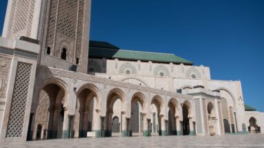 Ground-level mosque arcade with tall pointed arches, carved stone, lattice panels, and green lower trim.