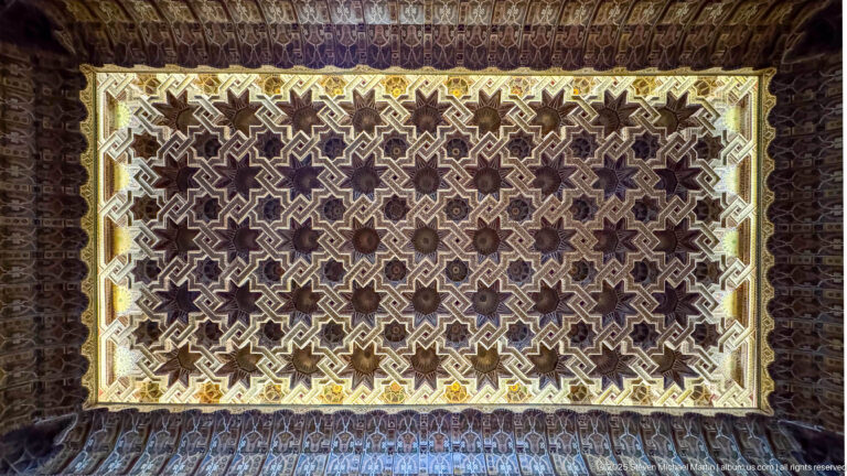 Illuminated rectangular ceiling panel with dense interlocking stars and stepped polygons framed by darker carved ornament.