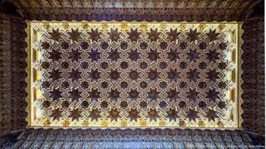 Illuminated rectangular ceiling panel with dense interlocking stars and stepped polygons framed by darker carved ornament.