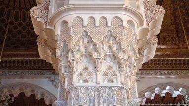 Close view of a monumental muqarnas-style capital with tiered niche-like carving beneath mosque arches.