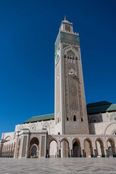 Low-angle close view of the patterned minaret above a row of large entrance arches.