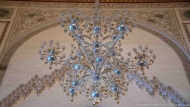 Large branching chandelier hangs in front of a richly decorated arch with scalloped and geometric ornament.