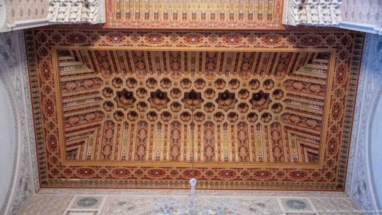 Rectangular carved and painted wooden ceiling with repeating coffers, rosettes, geometric motifs, and ornate border.