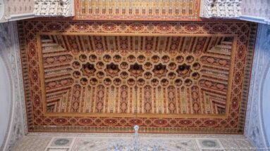 Rectangular carved and painted wooden ceiling with repeating coffers, rosettes, geometric motifs, and ornate border.