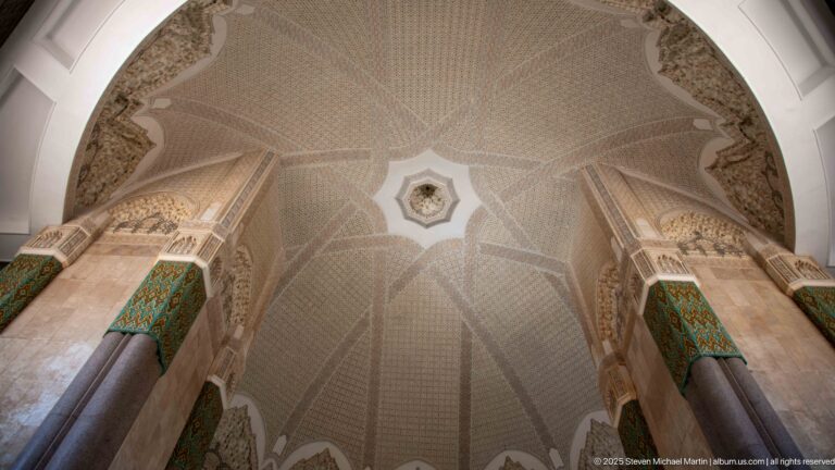 Upward view of a broad patterned vault spanning between monumental stone columns with green decorative panels.