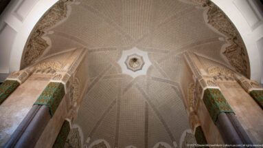 Upward view of a broad patterned vault spanning between monumental stone columns with green decorative panels.
