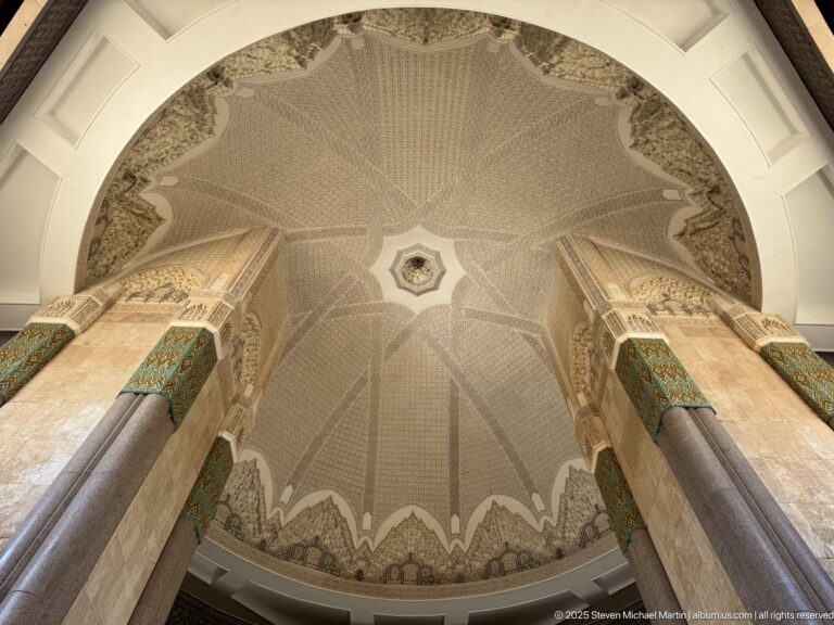 Symmetrical upward view of patterned mosque vault between two monumental stone columns with green decorative bands.