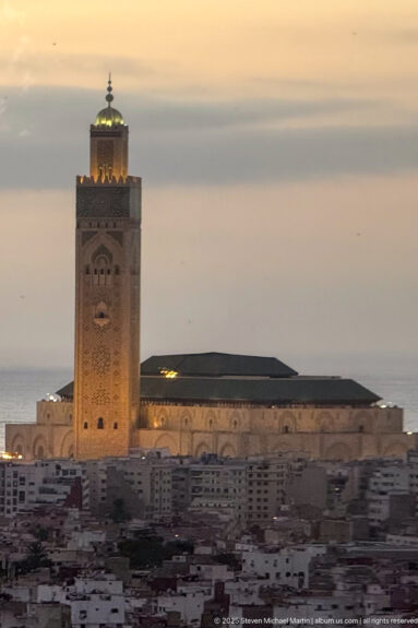 Illuminated Hassan II Mosque minaret rises above Casablanca at dusk with the Atlantic horizon behind it.