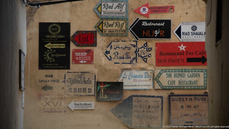 Cluster of colorful directional signs and arrows for riads, restaurants, cafés, museums, and guesthouses on a medina wall.