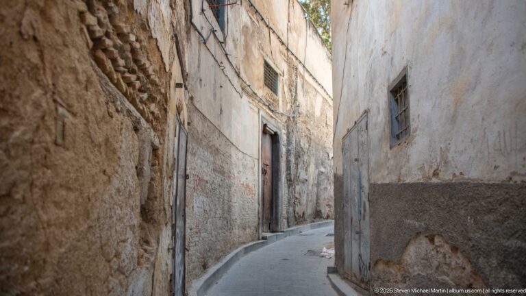 Curving narrow medina lane between weathered plaster and masonry walls with small windows and doors.