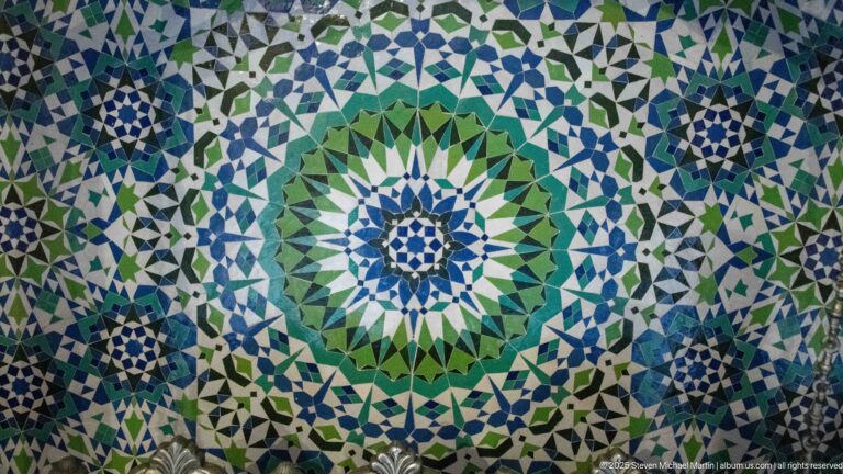 Close-up of green, blue, white, and black zellij forming a large radial star medallion with smaller surrounding motifs.