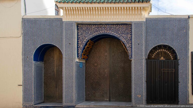 Symmetrical three-door façade with a large central horseshoe arch framed by blue-and-white zellij.