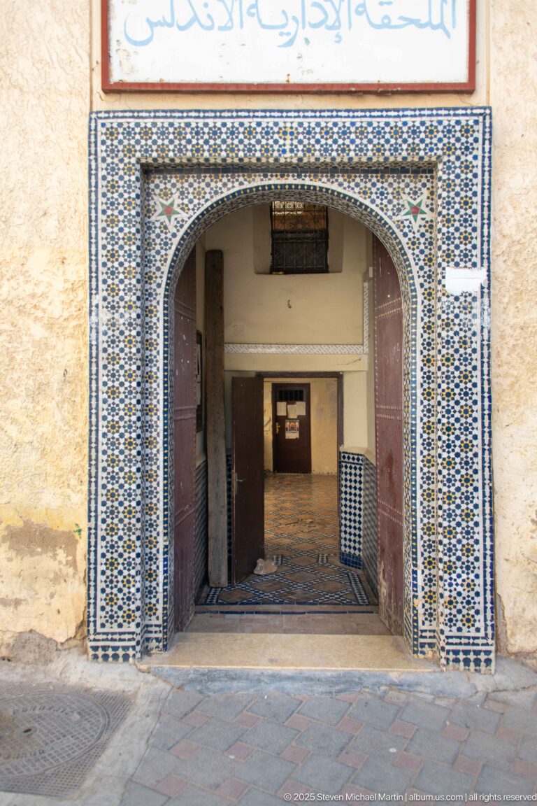 Wide horseshoe-arched entrance framed by blue, white, green, and ochre geometric zellij tilework.