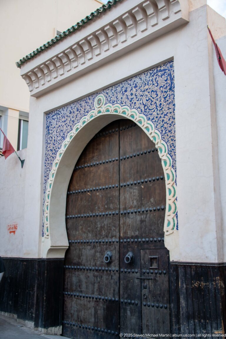 Large studded double wooden gate beneath a horseshoe arch edged with blue-and-white tilework and green trim.