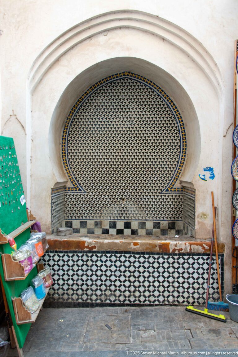 Recessed horseshoe-arched wall fountain with fine mosaic tile and a black-and-white tiled basin.