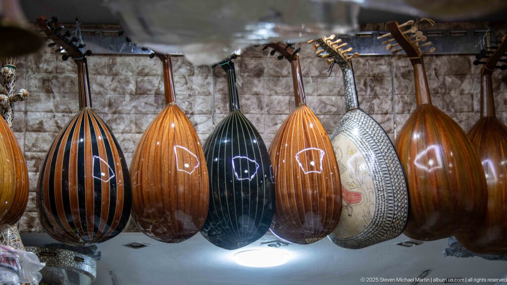 Row of pear-shaped wooden ouds hanging in a shop, with striped ribs, dark finishes, and decorative inlay.