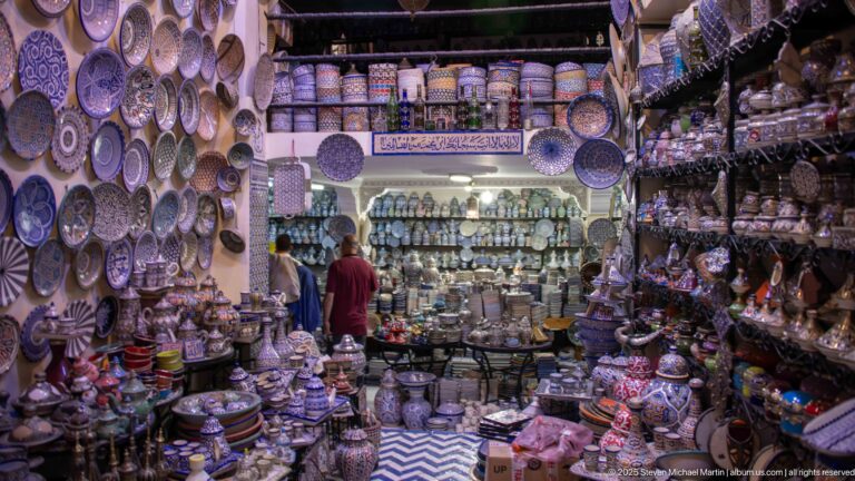 Narrow ceramics shop densely filled with painted bowls, plates, tagines, jars, and other colorful pottery.