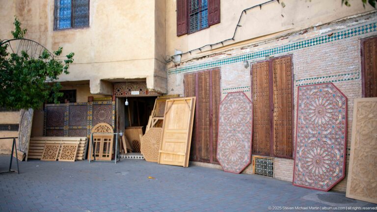 Decorative wooden doors, panels, and carved screens displayed outside a medina woodworking shop.