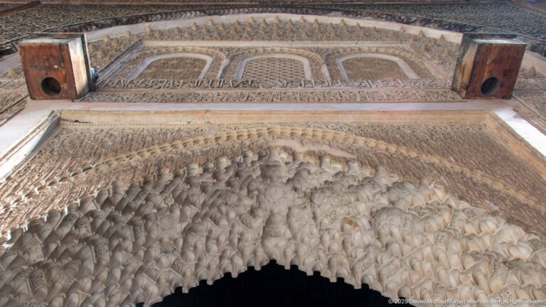 Close upward view of deeply carved muqarnas forming a honeycomb-like arch beneath bands of pale plaster ornament.