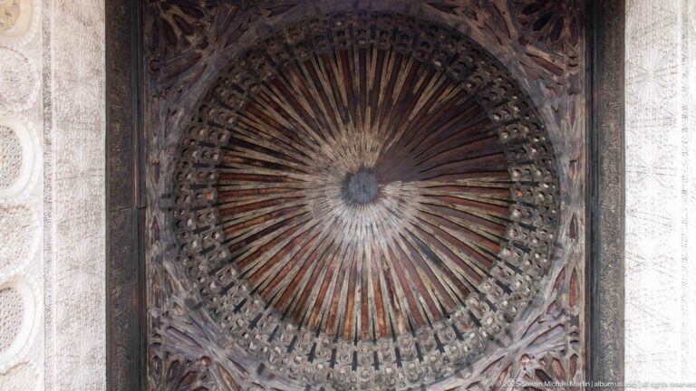 Circular carved wooden ceiling with radial ribs and concentric ornament spreading outward from a central boss.