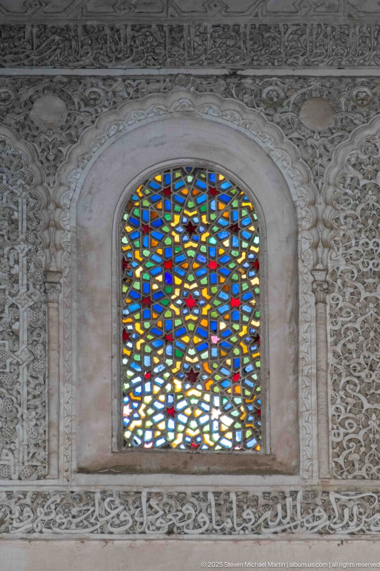 Rounded arched window with blue, red, yellow, and green geometric glass amid intricate carved plaster.
