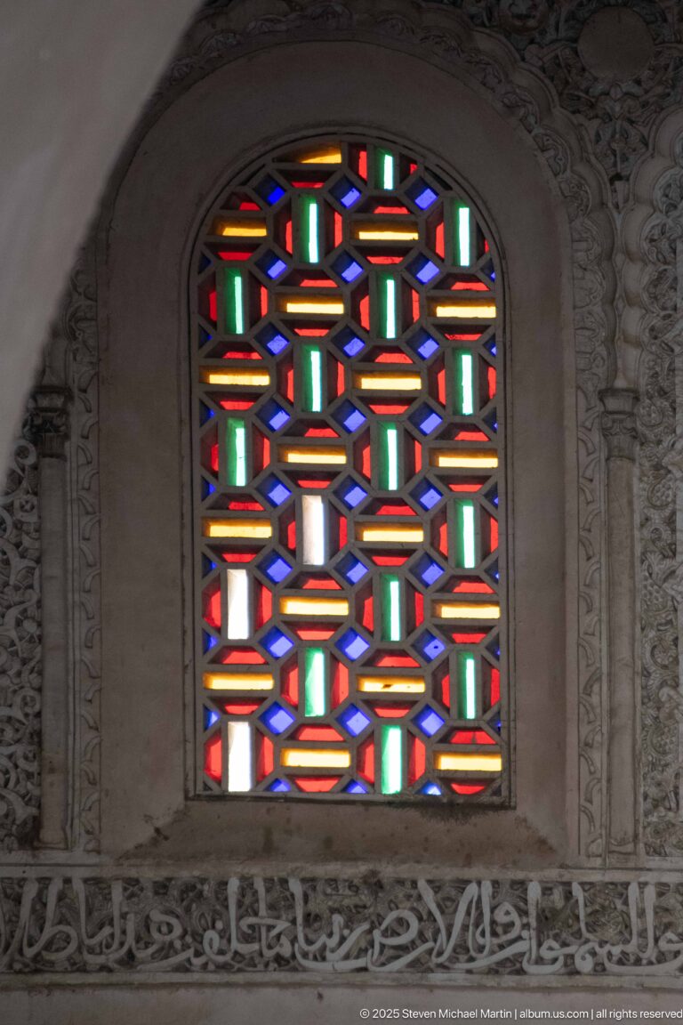 Close view of an arched geometric window with red, green, blue, amber, and white glass.