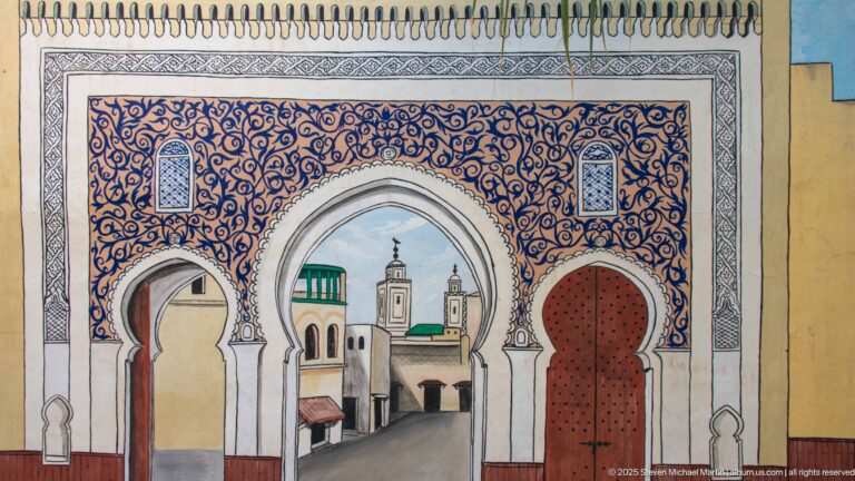 Colorful wall mural of Moroccan arches framing a painted medina street and towers.