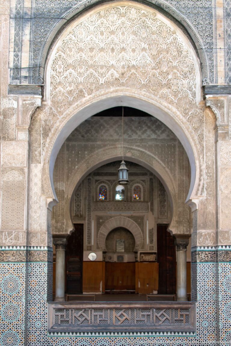 Large horseshoe arch framing columns, smaller arches, wood paneling, tilework, and a hanging lantern in an interior bay.
