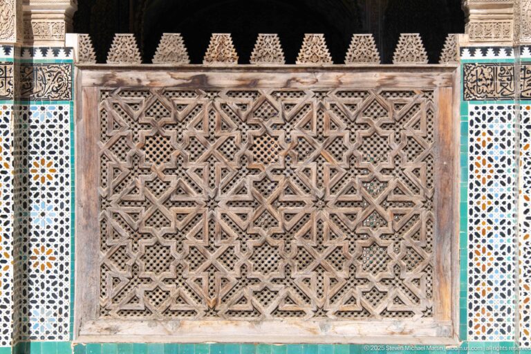 Large geometric pierced wooden screen bordered by narrow multicolored zellij panels and decorative bands.
