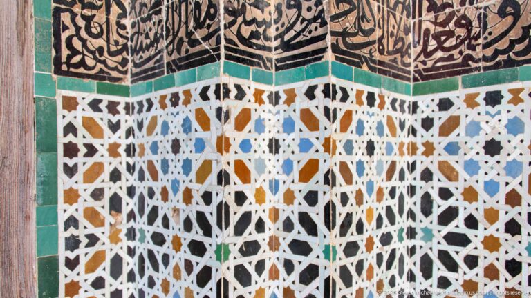 Corner covered with multicolored geometric zellij beneath a dark calligraphic decorative band.