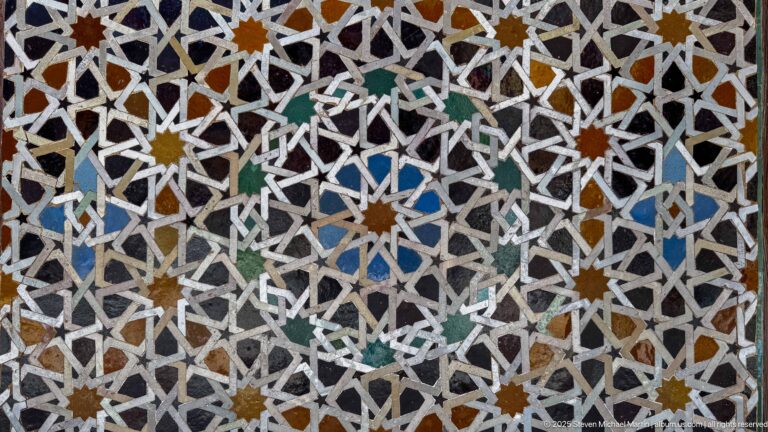 Dense geometric zellij close-up with white interlacing lines and small multicolored stars and polygons.
