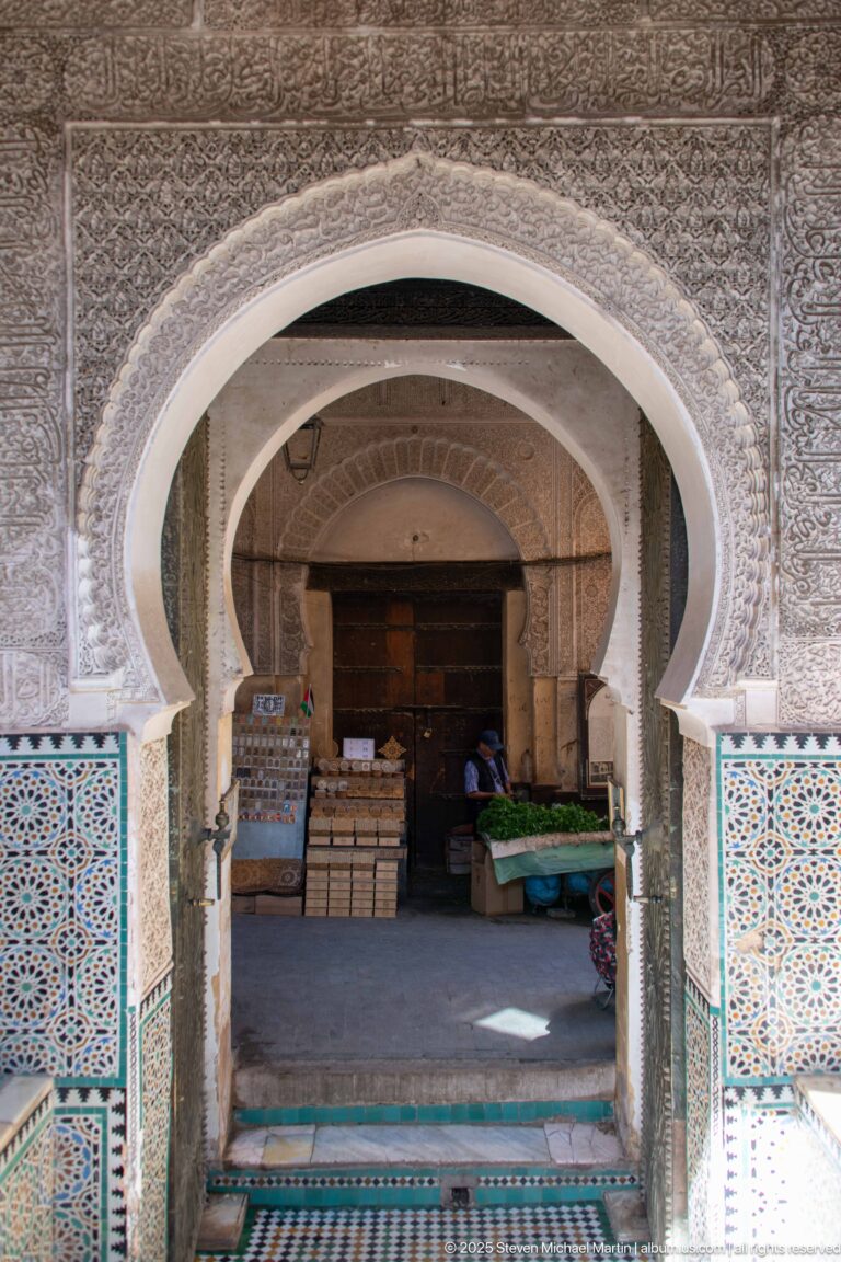Decorated horseshoe arch and tiled walls opening toward an interior space with stacked goods and covered tables.