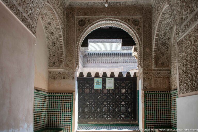 Horseshoe arch framed by carved stucco above a green zellij dado, with a dark wooden screen beyond.
