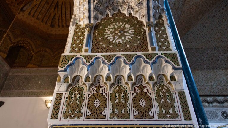 Decorated vertical support with miniature scalloped arches, painted panels, circular medallion, and blue edging.