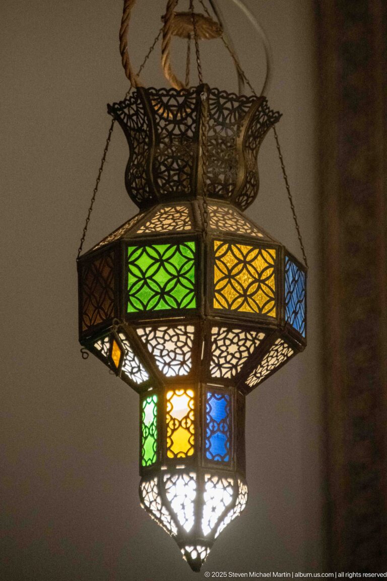 Pierced metal hanging lantern with green, amber, blue, and clear glass panels suspended by chains.