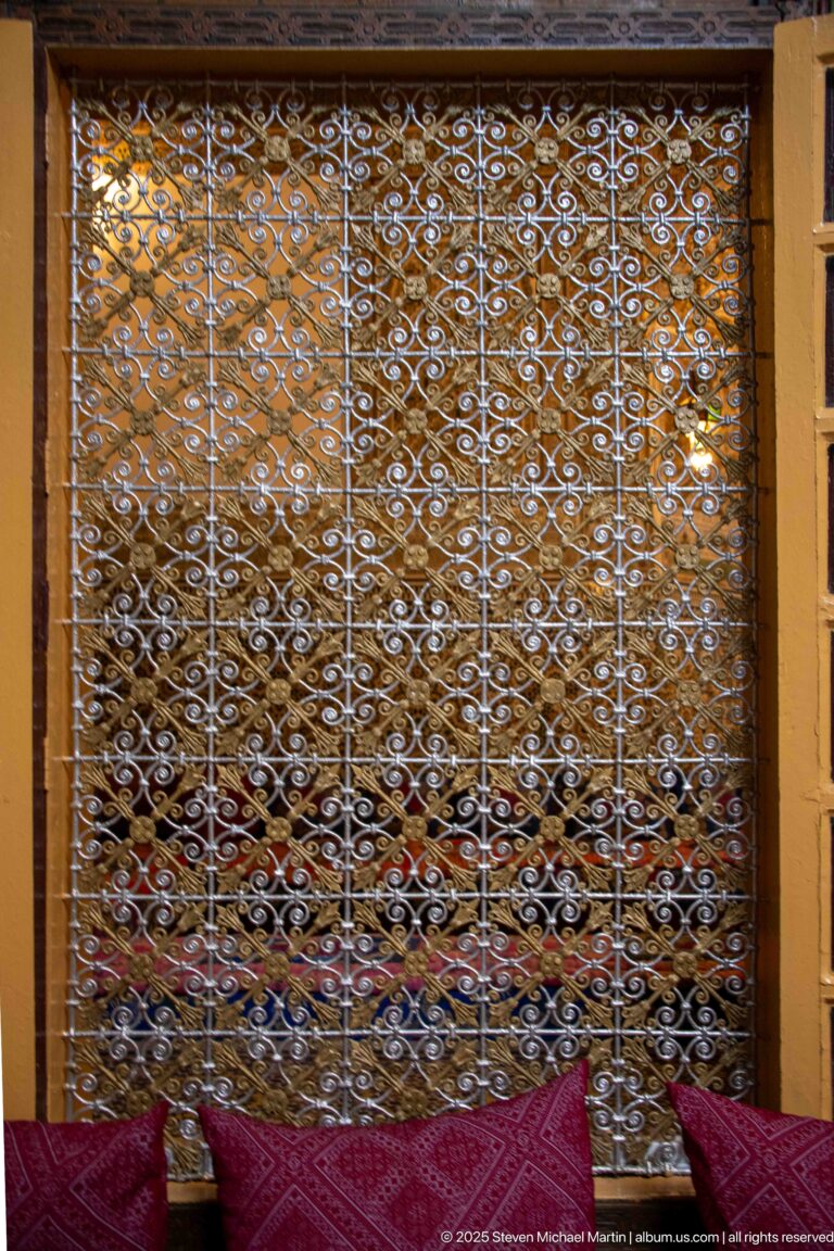 White ornamental metal lattice above low red and patterned seating in a Palais Mnebhi reception room.