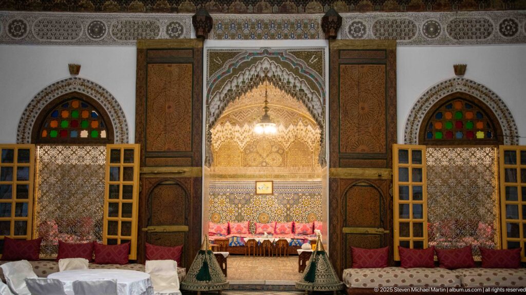 Frontal salon wall with central carved seating alcove, matching colored-glass windows, wooden shutters, and carved panels.