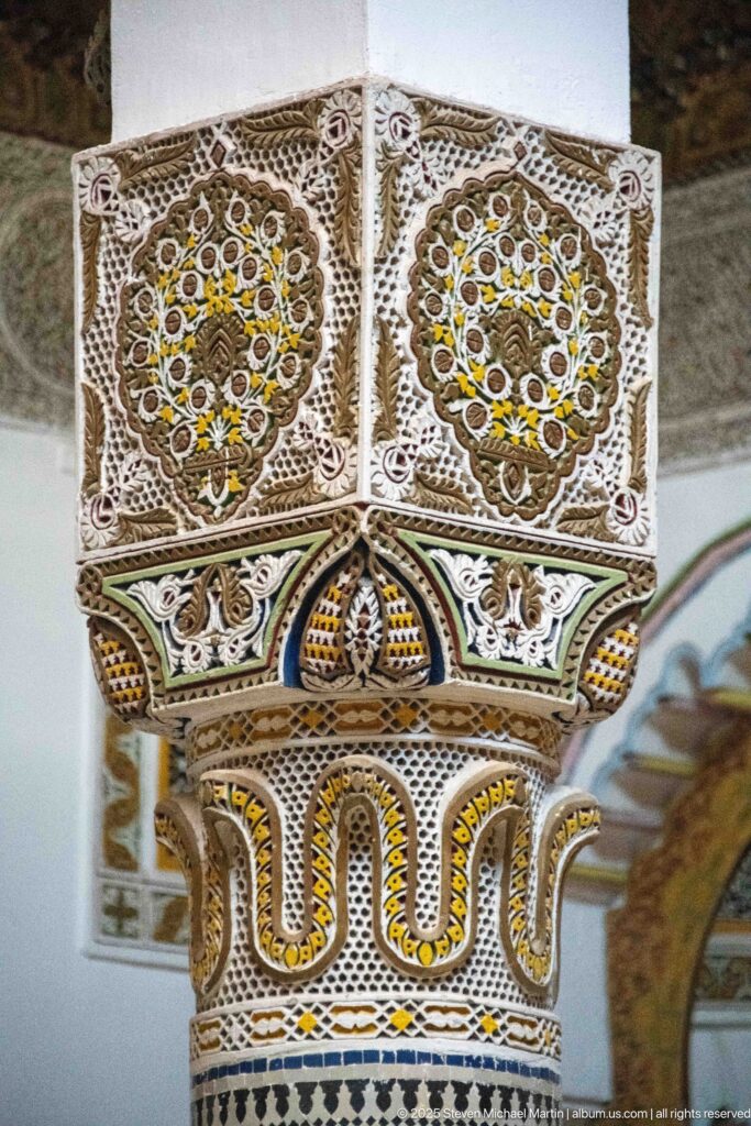 Detailed square capital with two circular floral medallions, multicolored accents, lace-like carving, and scalloped lower band.