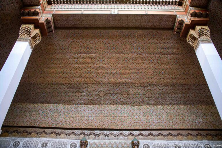 Wide upward view of a painted ceiling densely covered with repeating geometric rosettes between white structural supports.