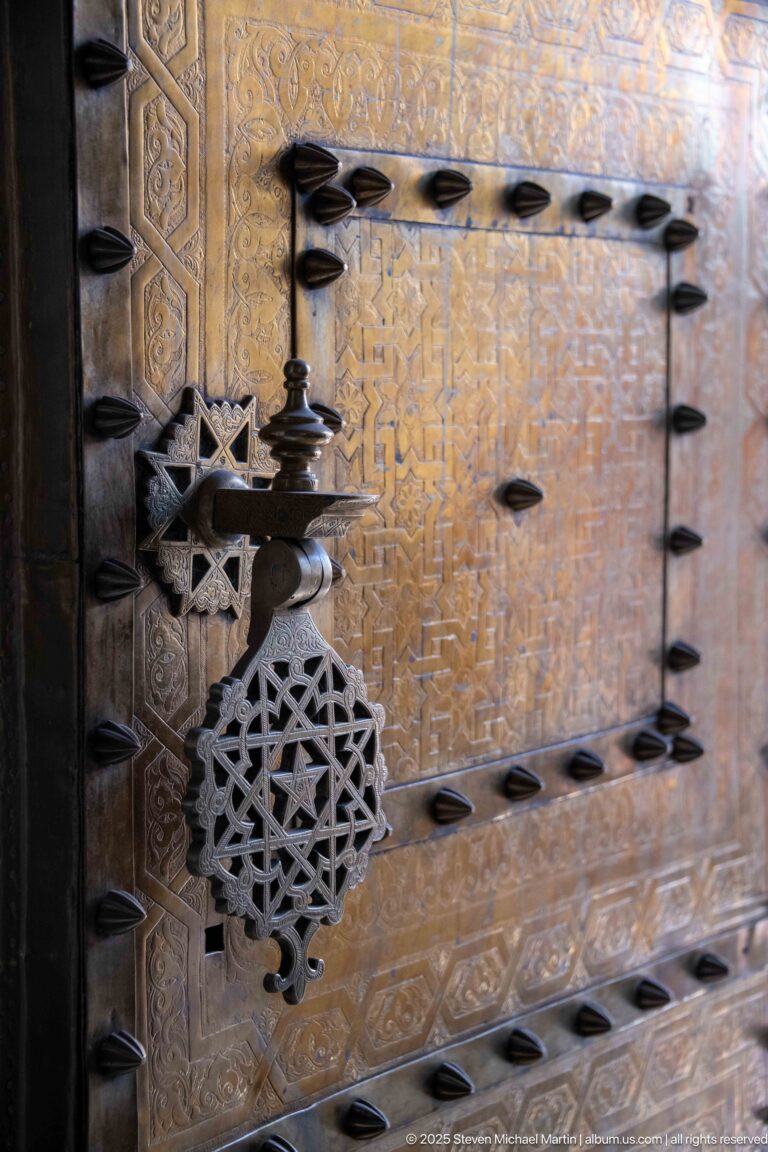 Carved wooden door with rows of dark metal bosses and an elaborate projecting star-shaped metal knocker.