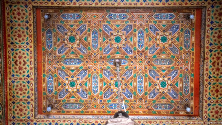 Rectangular painted ceiling panel filled with interlocking stars and polygons in turquoise, blue, red, green, ochre, and white.