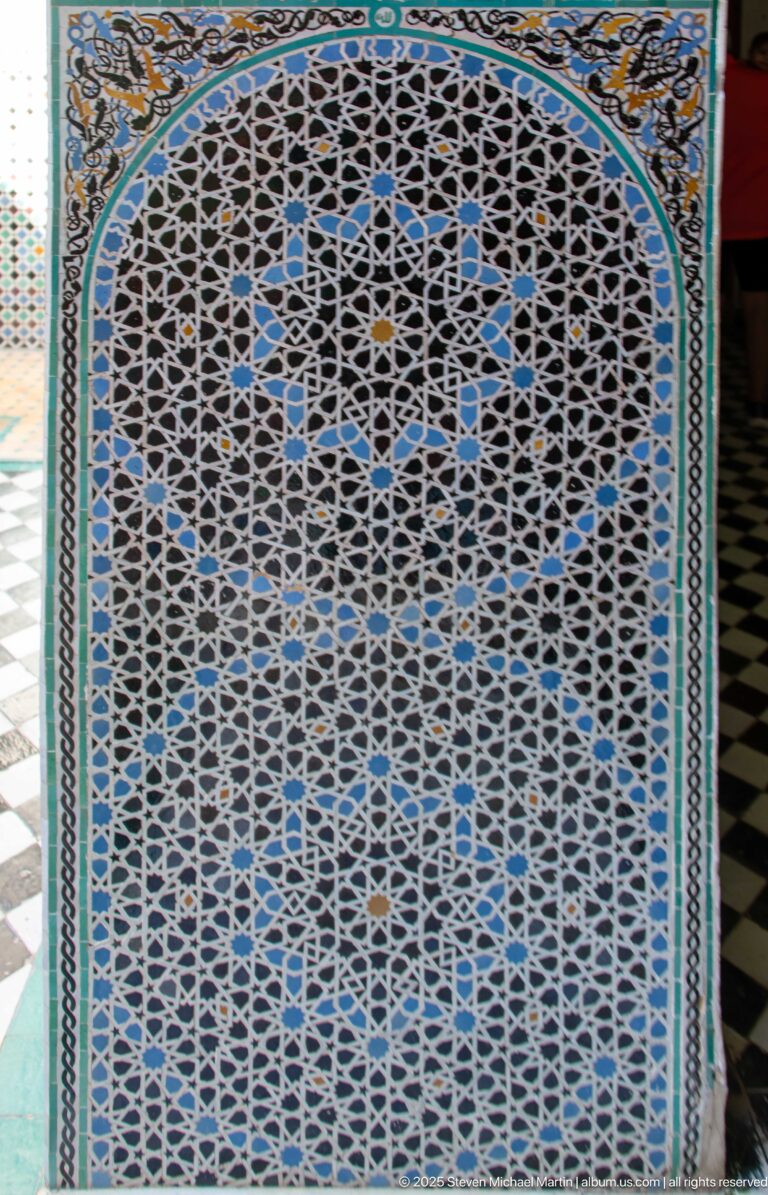 Close view of blue, black, white, and ochre zellij arranged as interlocking stars and polygons within a patterned border.