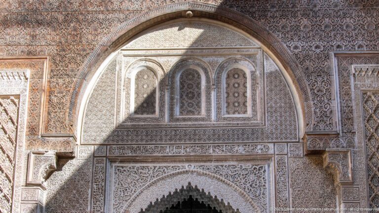 Upper Attarine Madrasa façade with three narrow windows, deeply carved stucco arch, and dense geometric and vegetal ornament.